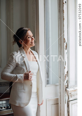 a beautiful, confident woman in a white suit at the old window. image of bride 97532049