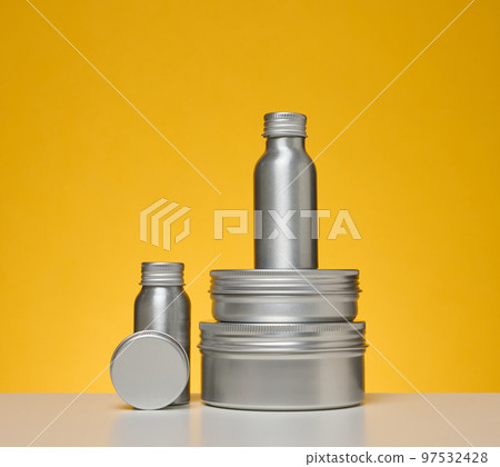Empty silver metal bottle for cosmetics on white table, yellow background. Packaging for cream Empty silver metal bottle for cosmetics on white table, yellow background. Packaging for cream 97532428