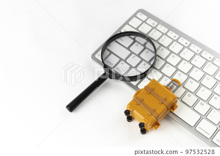 在計算機上預訂旅行的圖像。一個鍵盤，一個手提箱和一個放大鏡。 97532528