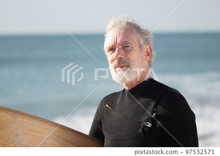 Portrait of sporty aged man resting on shore after surfing 97532571