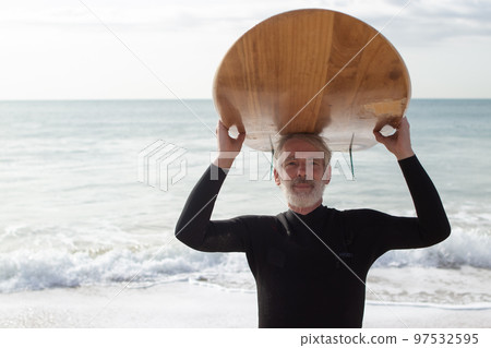 Portrait of happy elderly surfer carrying surfboard Portrait of happy elderly surfer carrying surfboard 97532595