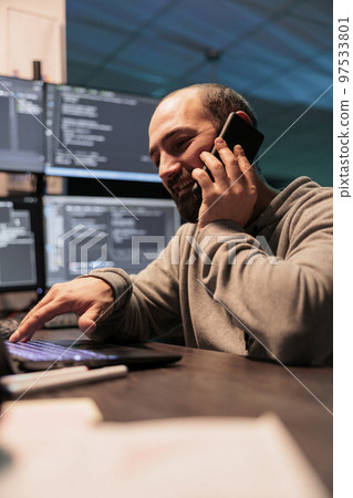 System engineer answering phone call late at night, talking to coders on smartphone and programming html script. Chatting on mobile phone and developing new it source code. System engineer answering phone call late at night, talking to coders on smartphone and programming html script. Chatting on mobile phone and developing new it source code. 97533801
