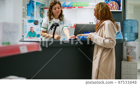 African american constumer buying pharmaceutical products and paying with debit card at pharmacy counter. Using contactless payment to buy medicaments and healthcare supplements at drugstore. 97533848
