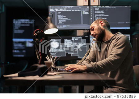 Software engineer talking on landline phone call after hours, answering office cord telephone to program code on terminal window. Database admin using phone line to develop new interface. Software engineer talking on landline phone call after hours, answering office cord telephone to program code on terminal window. Database admin using phone line to develop new interface. 97533889
