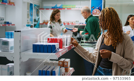 Young adult looking at boxes of medicaments to cure disease, having prescription treatment and checking supplements packages on shelves. Buying medicaments and pills from pharmacy shop. 97533965