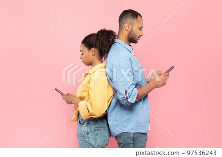 Social network addiction. African american couple using smartphones, standing back to back, pink background 97536243