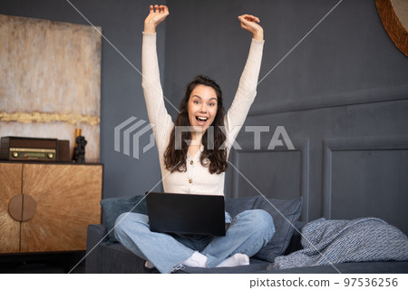 Excited woman celebrating success, raising hands up, sitting on sofa with laptop and reading great news, screaming yes Excited woman celebrating success, raising hands up, sitting on sofa with laptop and reading great news, screaming yes 97536256
