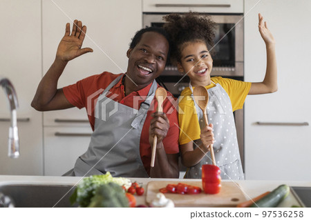Cheerful black father and preteen daughter having fun while cooking in kitchen Cheerful black father and preteen daughter having fun while cooking in kitchen 97536258