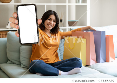 Mobile Ad. Smiling Middle Eastern Female Demonstrating Blank Smartphone And Shopping Bags 97536289