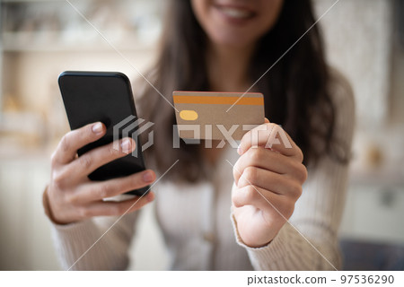 Lady with smartphone and credit card enjoy buying online, sitting at table in kitchen interior, selective focus 97536290