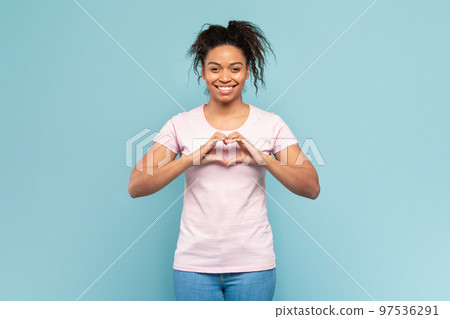 Cheerful black lady showing fingers heart gesture and smiling to camera, standing over blue studio background 97536291