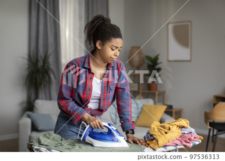 Unhappy tired millennial african american housewife iron clothes, suffer from a lot of work and household chores Unhappy tired millennial african american housewife iron clothes, suffer from a lot of work and household chores 97536313