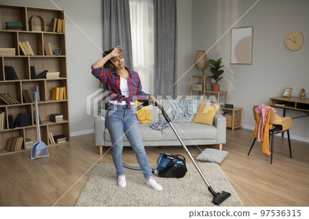 Tired sad millennial african american housewife wipes forehead and with vacuum cleaner, suffers from household chores Tired sad millennial african american housewife wipes forehead and with vacuum cleaner, suffers from household chores 97536315