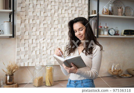 Young caucasian lady searching recipe for healthy dinner in cooking book, standing in kitchen interior, free space Young caucasian lady searching recipe for healthy dinner in cooking book, standing in kitchen interior, free space 97536318
