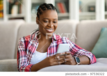 Cheerful beautiful black woman using smartphone at home Cheerful beautiful black woman using smartphone at home 97536322