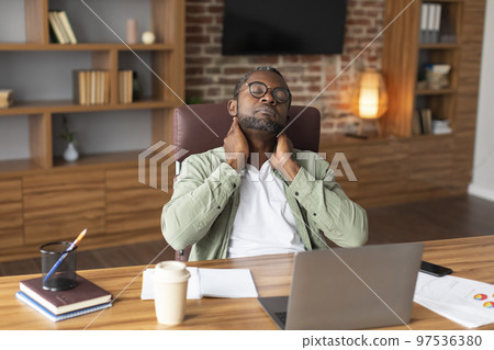 Tired adult black businessman in glasses suffering from neck pain, discomfort long hours of sedentary 97536380