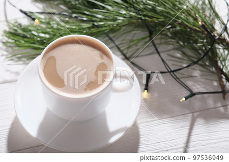cup of coffee with milk on a wooden table with pine tree branch and light garland decor. cozy christmas morning concept. cup of coffee with milk on a wooden table with pine tree branch and light garland decor. cozy christmas morning concept. 97536949