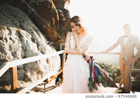 Young newly wed couple, bride and groom kissing, hugging on perfect view of mountains, blue sky 97540698