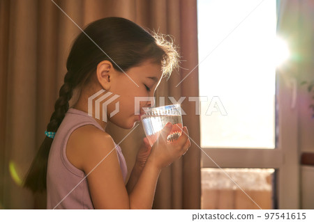 Girl drinks water from a glass in the sun. Back light. Girl drinks water from a glass in the sun. Back light. 97541615