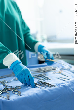 Vertical of midsection of surgical tech placing tools on table in operating theatre, with copy space Vertical of midsection of surgical tech placing tools on table in operating theatre, with copy space 97542381