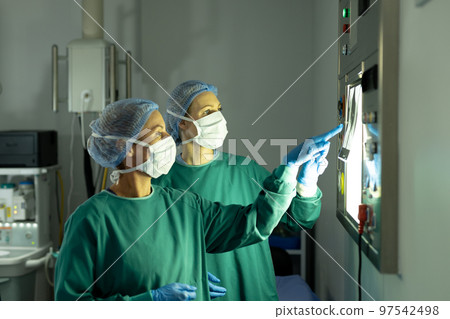 Two diverse female surgeons preparing for operation, studying x-ray in operating theatre Two diverse female surgeons preparing for operation, studying x-ray in operating theatre 97542498