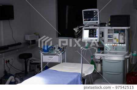 Electronic medical equipment with monitor screens on and empty operating table in operating theatre 97542513