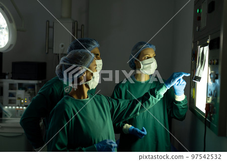 Three diverse surgeons preparing for operation, discussing x-ray in operating theatre Three diverse surgeons preparing for operation, discussing x-ray in operating theatre 97542532