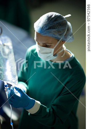 Vertical of caucasian female surgical tech preparing iv bag in operating theatre during opertion Vertical of caucasian female surgical tech preparing iv bag in operating theatre during opertion 97542566