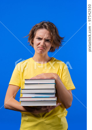 Lazy woman student is dissatisfied with amount of books homework on blue background. Girl with short Lazy woman student is dissatisfied with amount of books homework on blue background. Girl with short 97542930