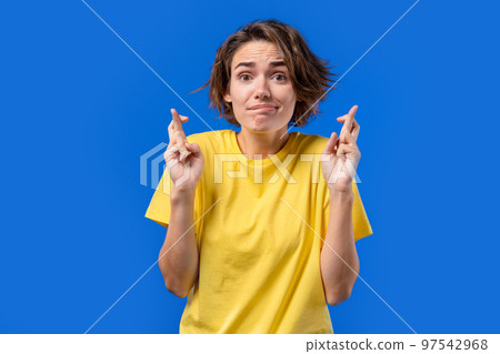 Pretty woman praying with crossed fingers on blue background. Lady begs someone satisfy her desires 97542968