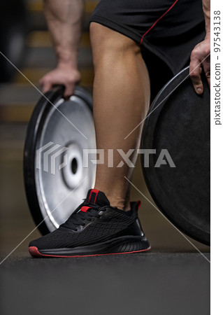 Muscular leg of a bodybuilder in a black sneaker on the gym Muscular leg of a bodybuilder in a black sneaker on the gym 97543138
