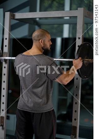 Athlete adding weight plates on his barbell 97543143