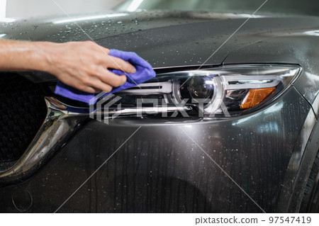 Crooped view of hand of male worker cleaning car headlights with blue microfiber cloth. 97547419