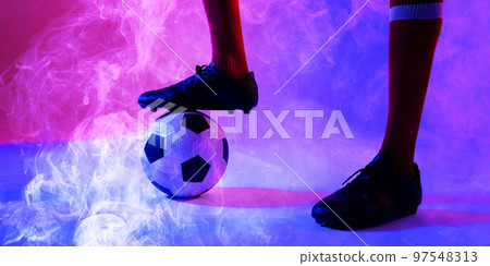 Low section of african american male player with leg on ball amidst smoky background 97548313
