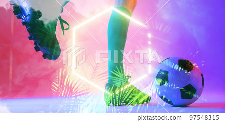 Low section of caucasian male player kicking ball by illuminated plants and hexagon, copy space 97548315