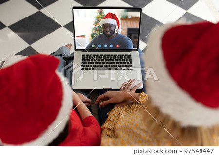 Caucasian mother and daughter in santa hats on christmas laptop video call with african american man 97548447