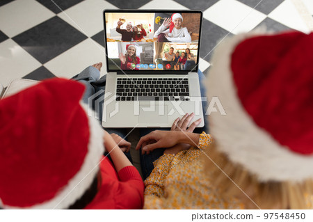 Caucasian mother and daughter in santa hats on christmas laptop video call with diverse friends Caucasian mother and daughter in santa hats on christmas laptop video call with diverse friends 97548450