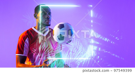 African american male soccer player with ball standing by illuminated square and plants African american male soccer player with ball standing by illuminated square and plants 97549399
