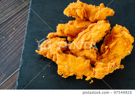 meat strips on a black tray. strips of meat fried in breading. meat strips on a black tray. strips of meat fried in breading. 97549928