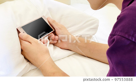 一個人的手看著枕頭上的智能手機 一個人的手看著枕頭上的智能手機 97553888