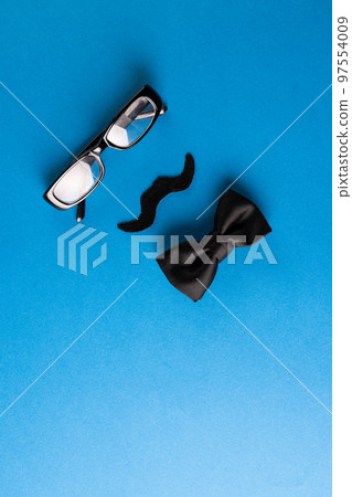 Composition of fake moustache with glasses and bow tie on blue background with copy space Composition of fake moustache with glasses and bow tie on blue background with copy space 97554009