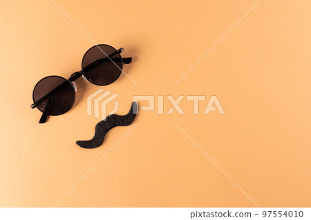 Composition of fake moustache and glasses on orange background with copy space 97554010