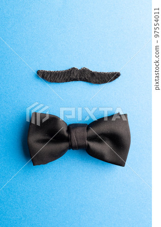 Composition of fake moustache and bow tie on blue background with copy space Composition of fake moustache and bow tie on blue background with copy space 97554011