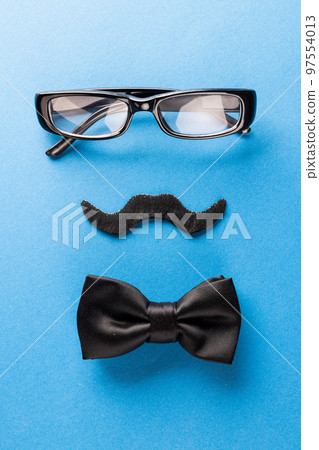 Composition of fake moustache with glasses and bow tie on blue background with copy space 97554013