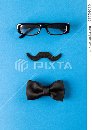 Composition of fake moustache with glasses and bow tie on blue background with copy space Composition of fake moustache with glasses and bow tie on blue background with copy space 97554029
