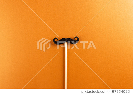 Composition of fake moustache on stick on orange background with copy space 97554033