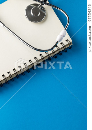 Vertical composition of stethoscope with notebook on blue background with copy space Vertical composition of stethoscope with notebook on blue background with copy space 97554246