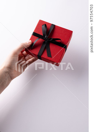 Vertical of hand giving red gift box tied with black ribbon, on white background with copy space 97554703