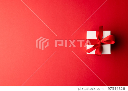 Overhead of white gift box tied with red ribbon, on red background with copy space 97554826