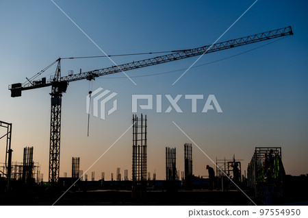 Industrial construction cranes and building silhouettes over sun at sunrise Industrial construction cranes and building silhouettes over sun at sunrise 97554950